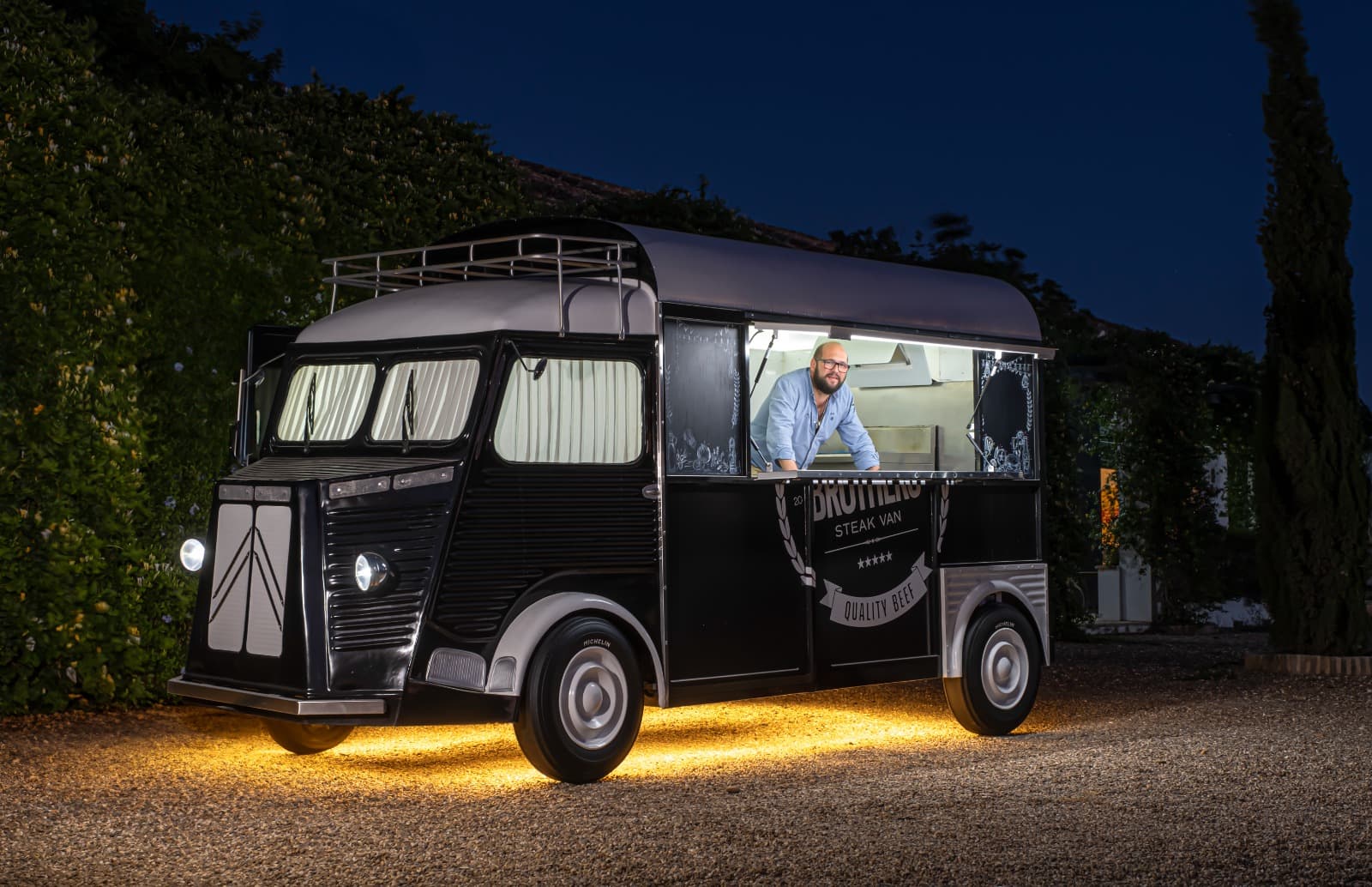 Food truck The Res Brothers Steak Van iluminada de noche con luces doradas, lista para un evento privado